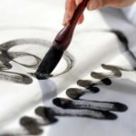 pexels-photo-9478289-9478289 Close-up of a hand using a calligraphy brush to apply black ink on white paper.